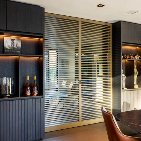Stijlvolle Anodic Bronze stalen schuifdeuren met glas en horizontale lamellen in een luxe interieur met donkere houten kasten.